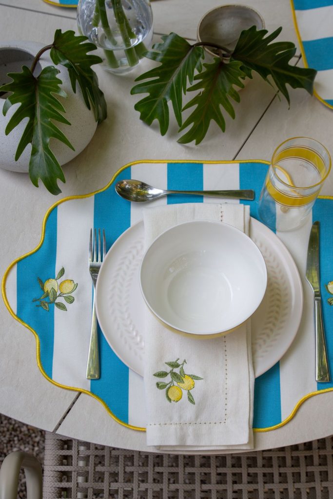 Foto ambientada de uma mesa com jogo americano e guardanapos com bordado de limão siciliano.