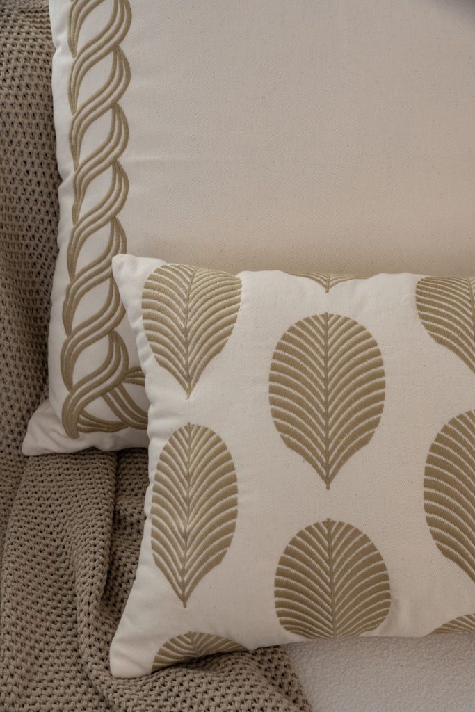 Detalhe de almofada bordada com padrões geométricos, linhas precisas e textura marcante